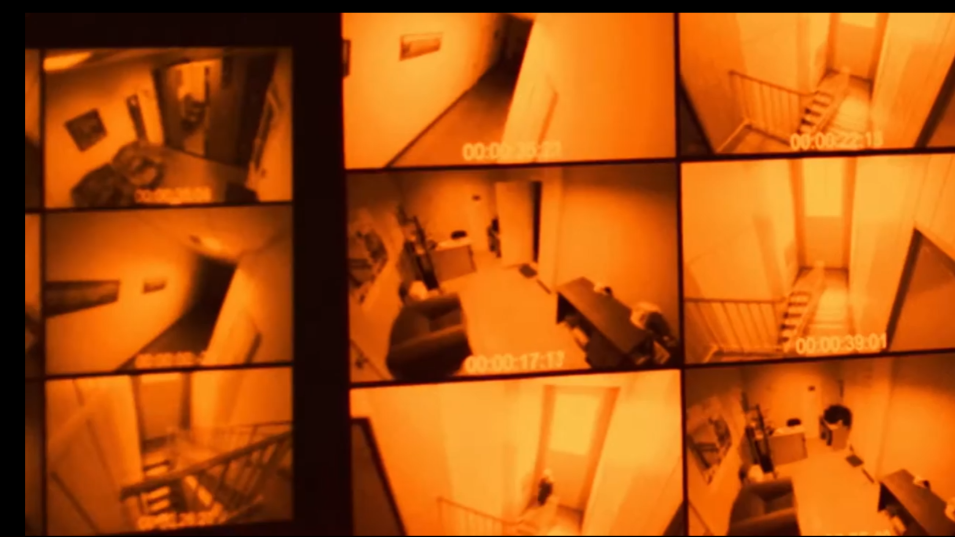 Split-screen security camera footage with various angles showing a dimly lit, orange-tinted hallway and stairwell, reminiscent of surveillance in a building.